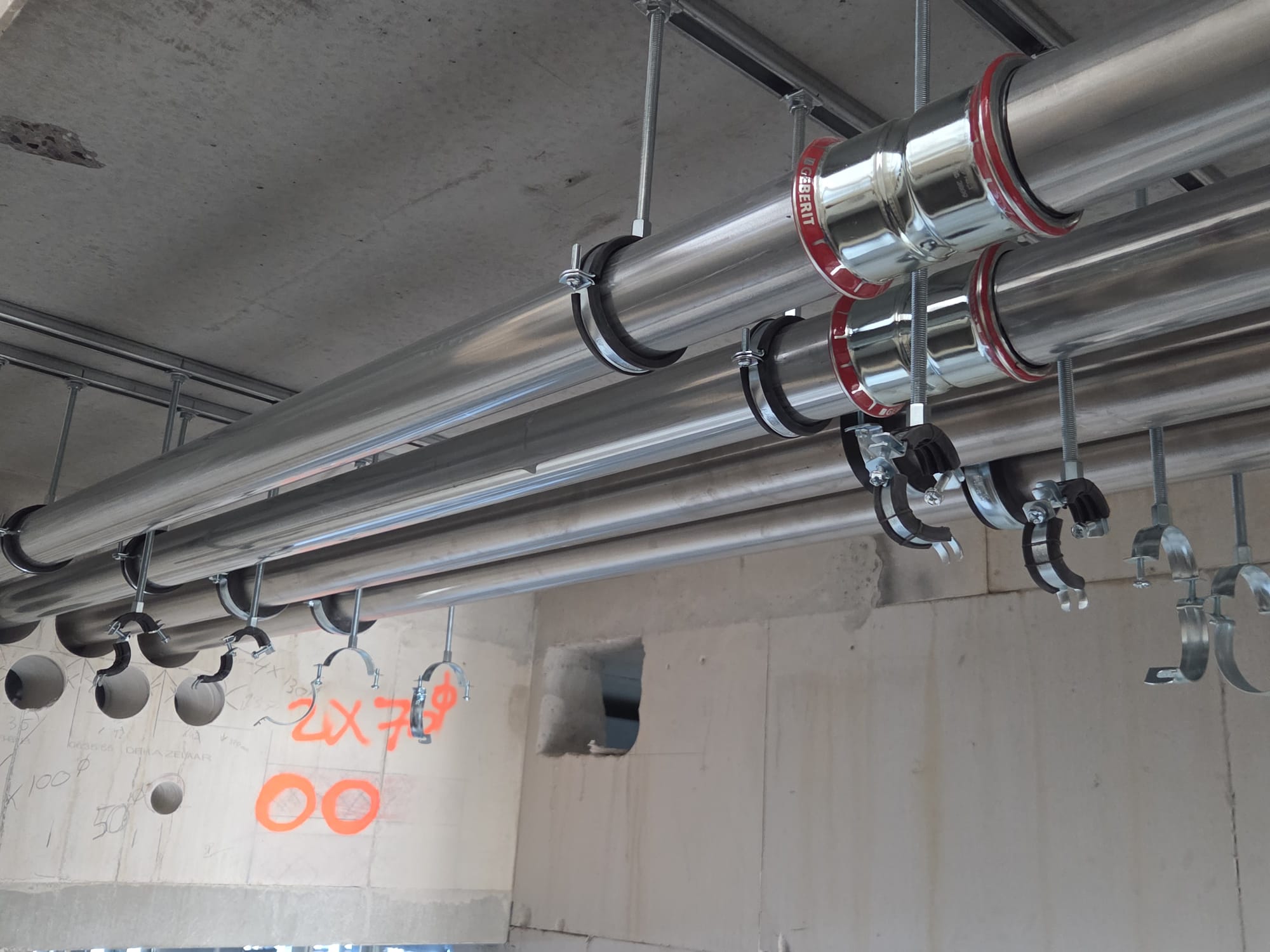 Installation of steel plumbing pipes mounted to a concrete ceiling.